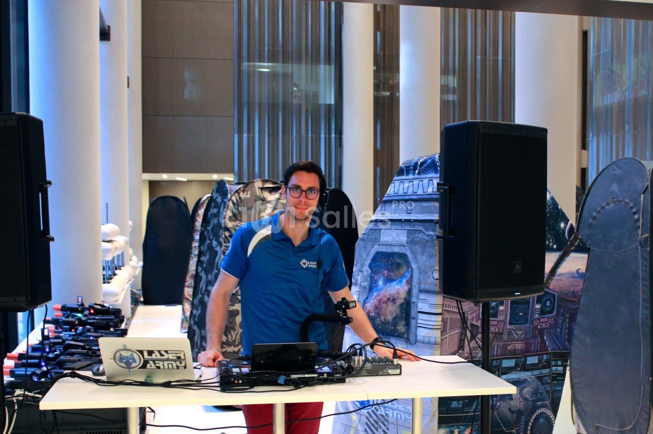 Un homme debout derrière une table équipée de matériel audio, dans un espace intérieur avec des décors futuristes.