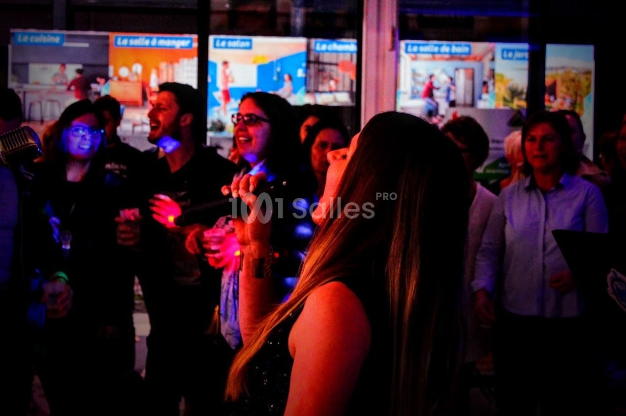 Une femme chante au micro devant un groupe de personnes dans un environnement lumineux et festif.