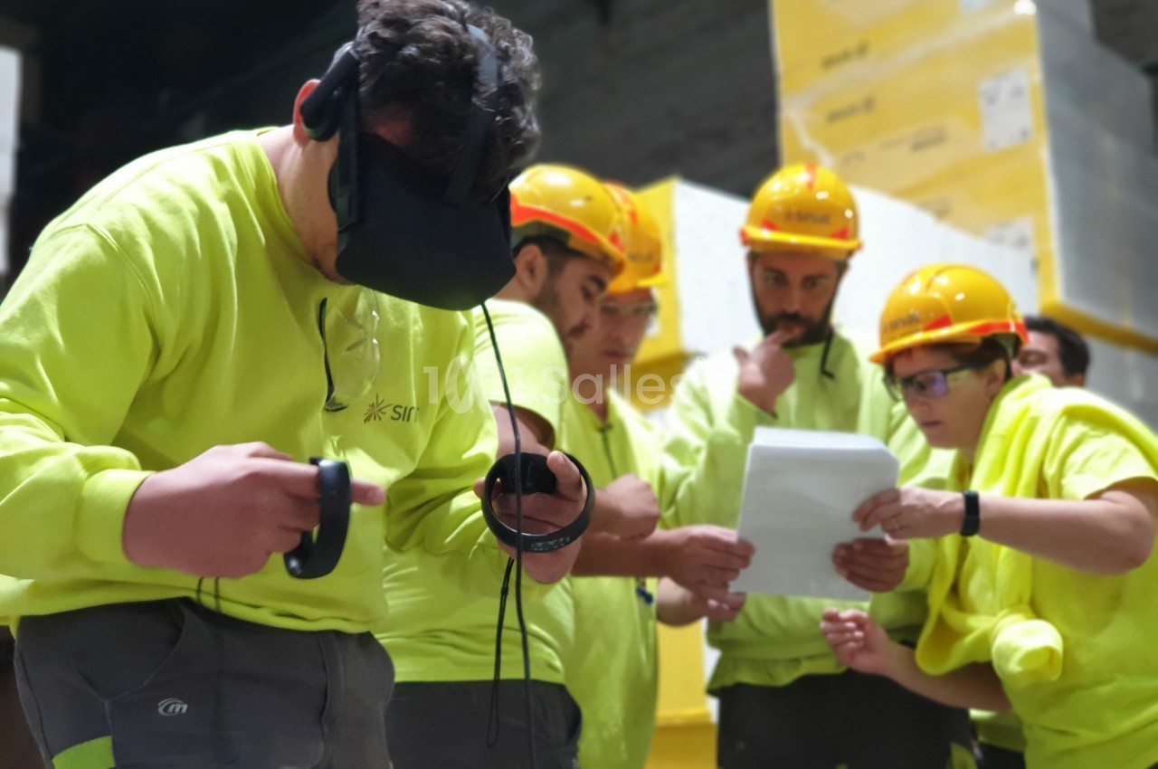Des ouvriers en tenue de sécurité utilisent un casque de réalité virtuelle et consultent des documents dans un entrepôt.