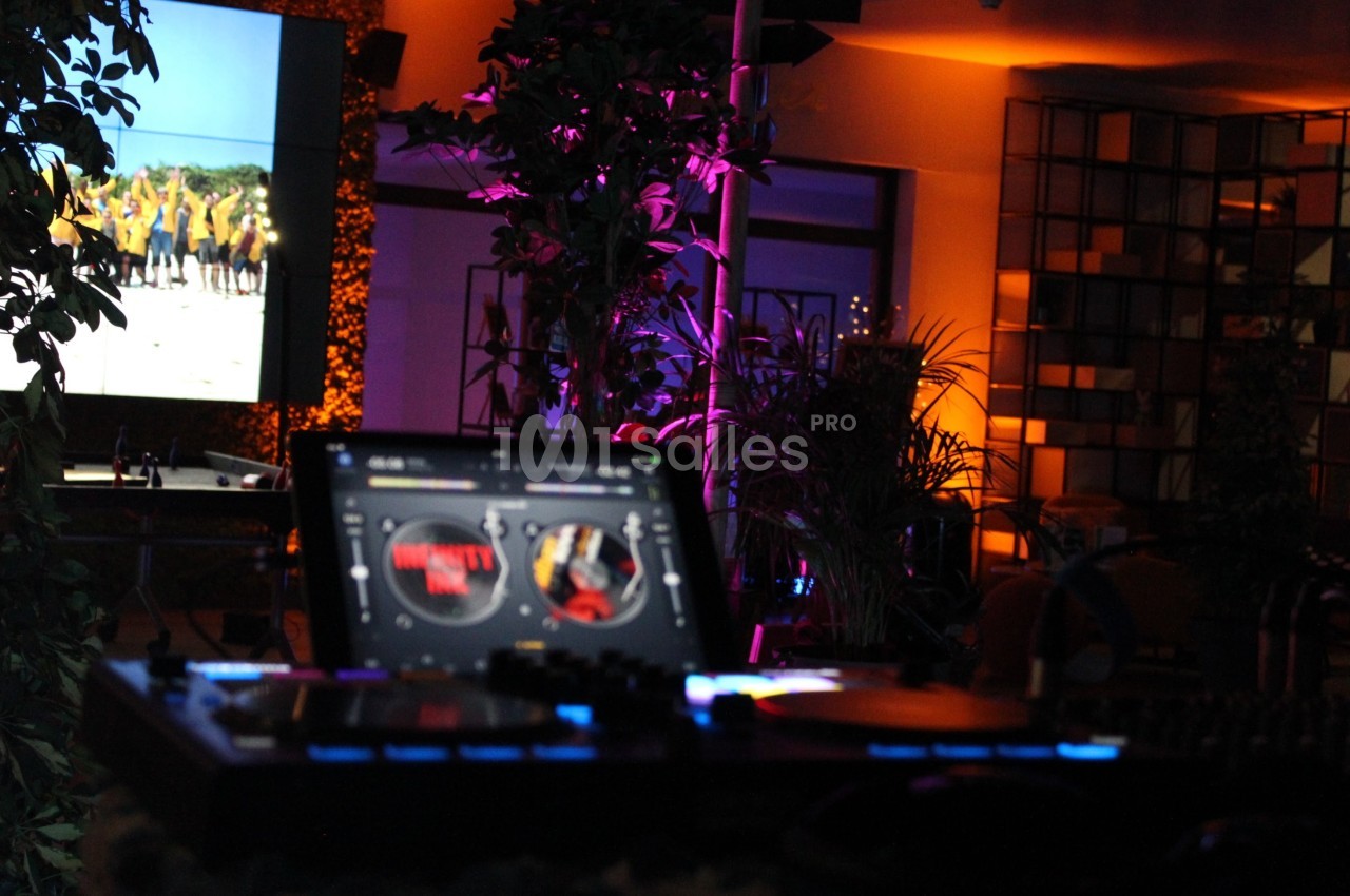 Poste de DJ avec platines éclairées au premier plan, écran et décor lumineux en arrière-plan.