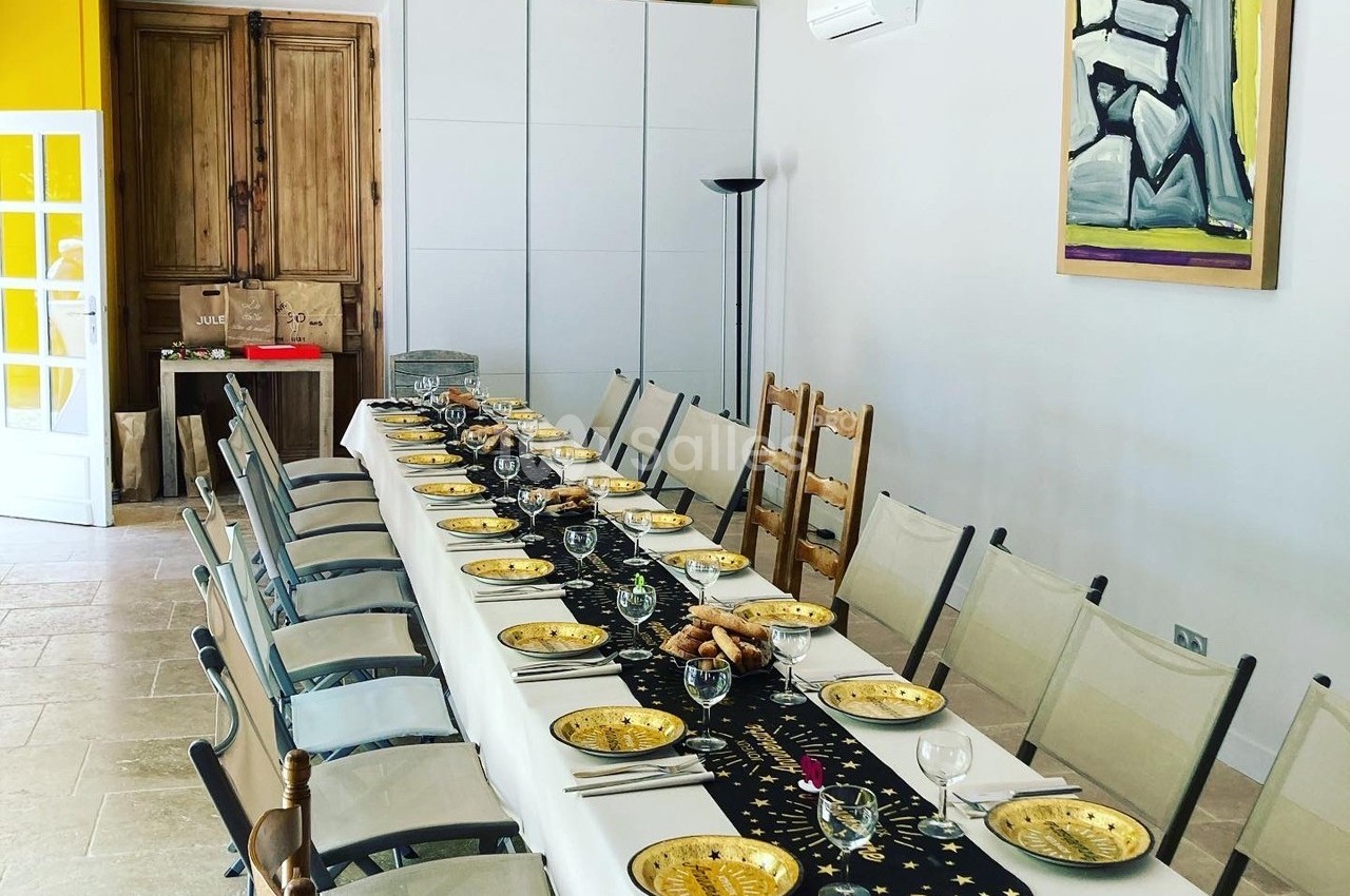Table dressée pour un repas, avec nappes blanches, assiettes dorées, chaises alignées et décoration sobre dans une salle…