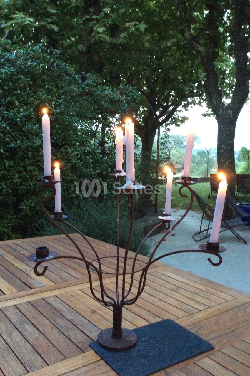 Chandelier en métal avec bougies allumées, posé sur une table en bois dans un jardin au crépuscule.