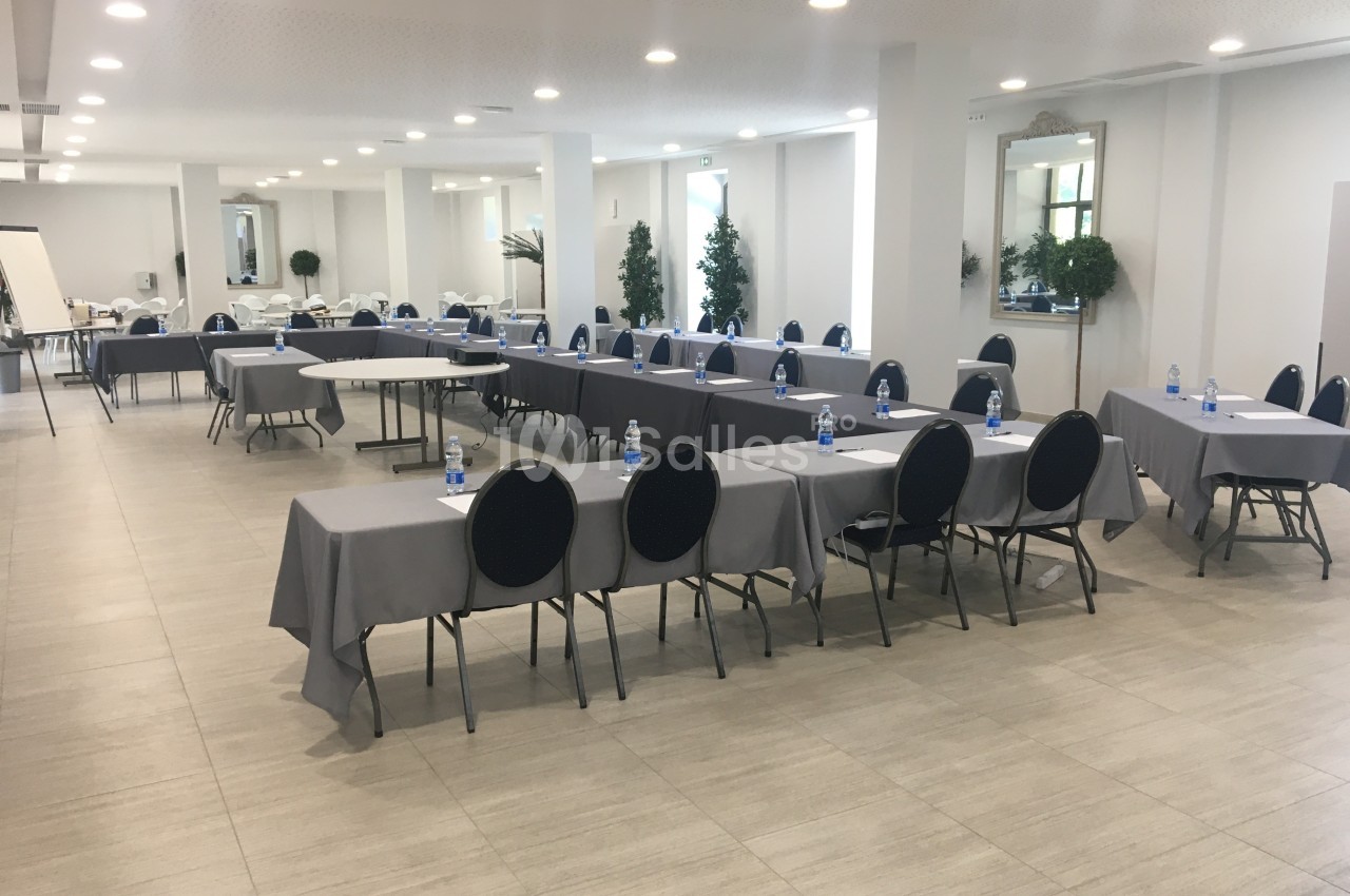 Salle de réunion lumineuse avec des tables disposées en U, chaises noires et bouteilles d'eau sur les tables.