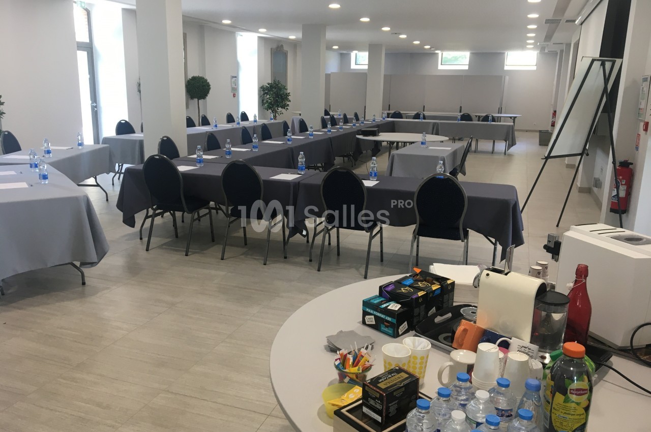Salle de réunion lumineuse avec tables disposées en U, chaises noires, et table de collation au premier plan.