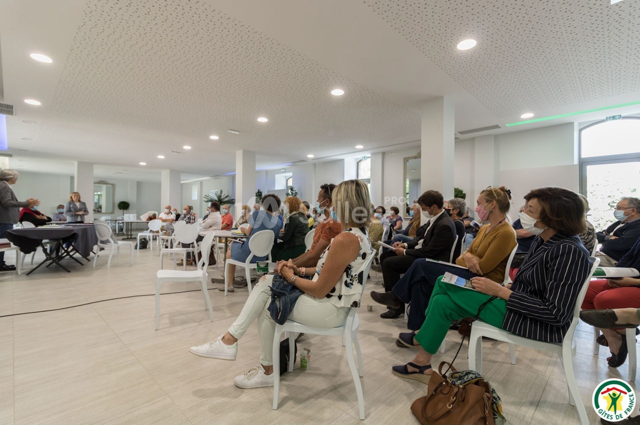 Personnes assises dans une salle de conférence lumineuse, écoutant une présentation.
