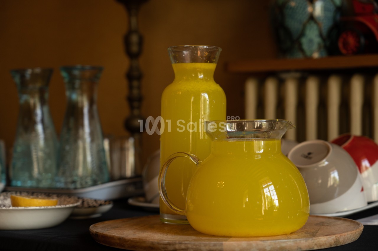 Carafes remplies de jus d'orange posées sur une table en bois, avec de la vaisselle en arrière-plan.