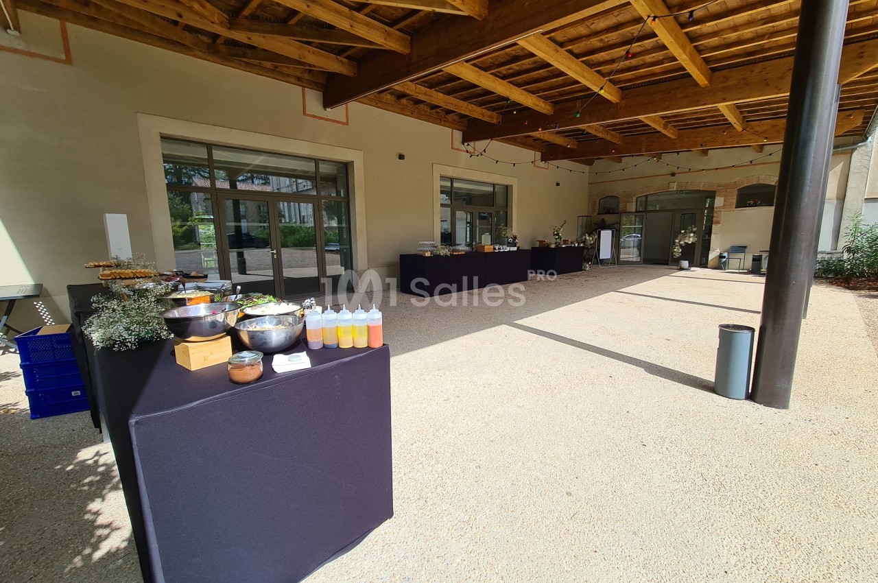 Tables de buffet dressées sous un auvent en bois, avec divers plats et condiments disposés sur des nappes noires.