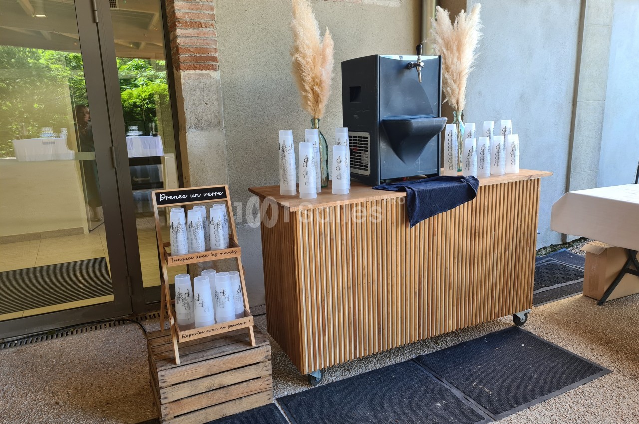 Distributeur d'eau avec bouteilles réutilisables en libre-service sur un comptoir en bois, décoré de pampas.