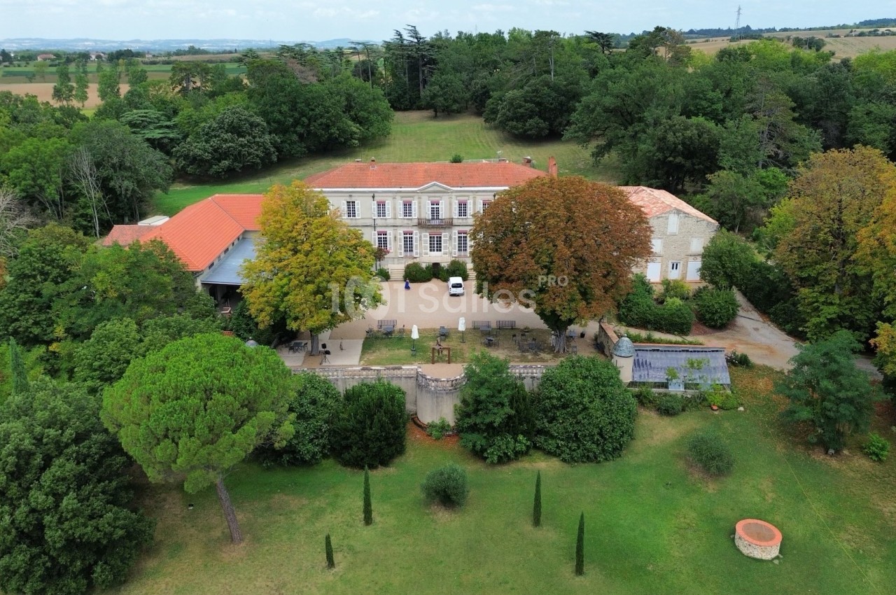 Vue aérienne d'un grand bâtiment ancien entouré de jardins verdoyants et d'arbres, dans un cadre rural.