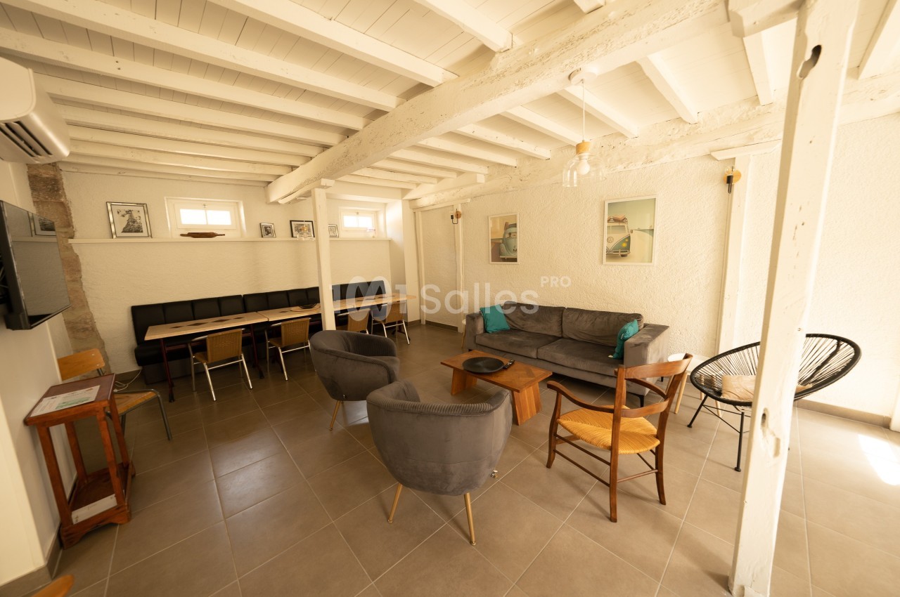 Salle de séjour lumineuse avec poutres apparentes, canapé, fauteuils, table à manger et décoration murale.