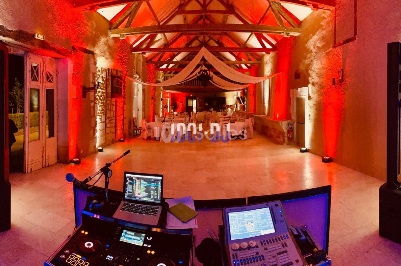Salle de réception décorée avec éclairage rouge et blanc, vue depuis une table de DJ équipée de matériel audio.