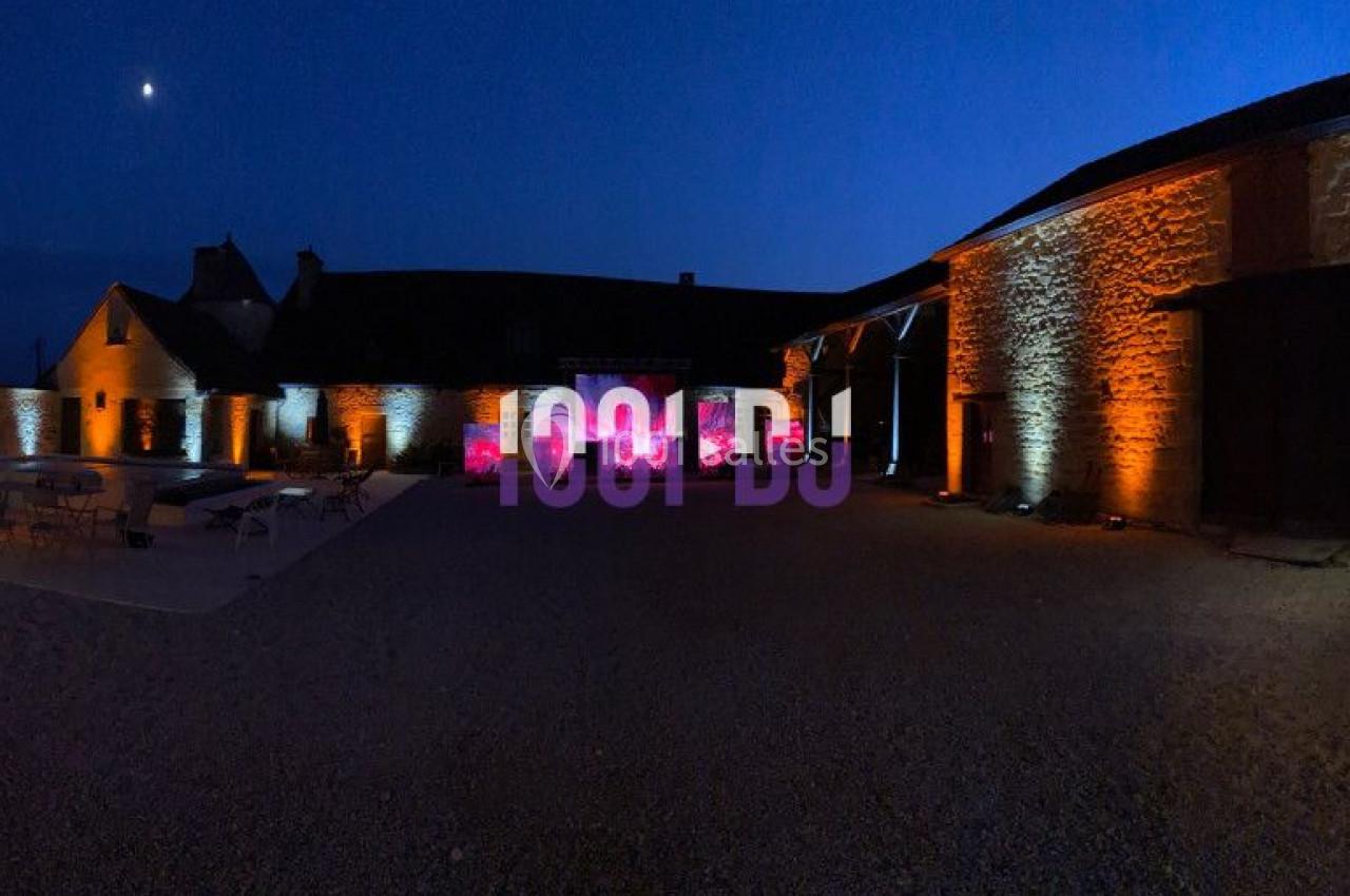 Cour intérieure d'un bâtiment en pierre éclairée par des lumières orange et violettes sous un ciel nocturne.