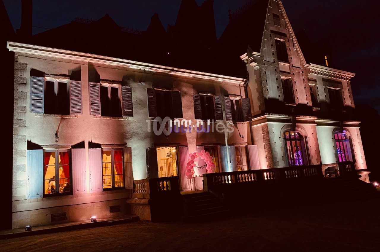 Façade d'un bâtiment ancien éclairé par des lumières colorées dans une ambiance nocturne.