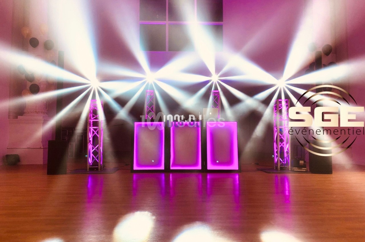 Installation lumineuse avec projecteurs LED colorés et panneaux lumineux violets dans une salle événementielle.