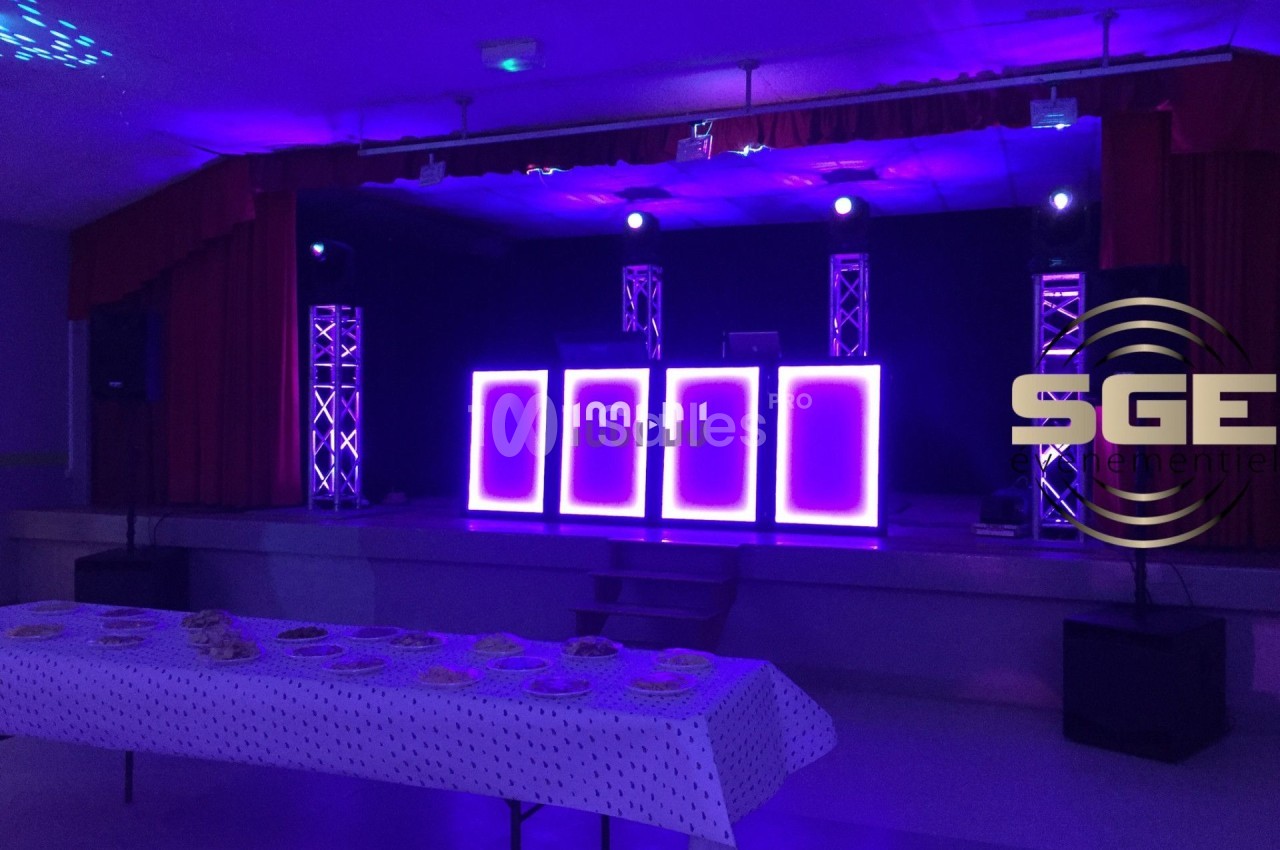 Scène éclairée en violet avec des équipements de sonorisation et une table dressée au premier plan.