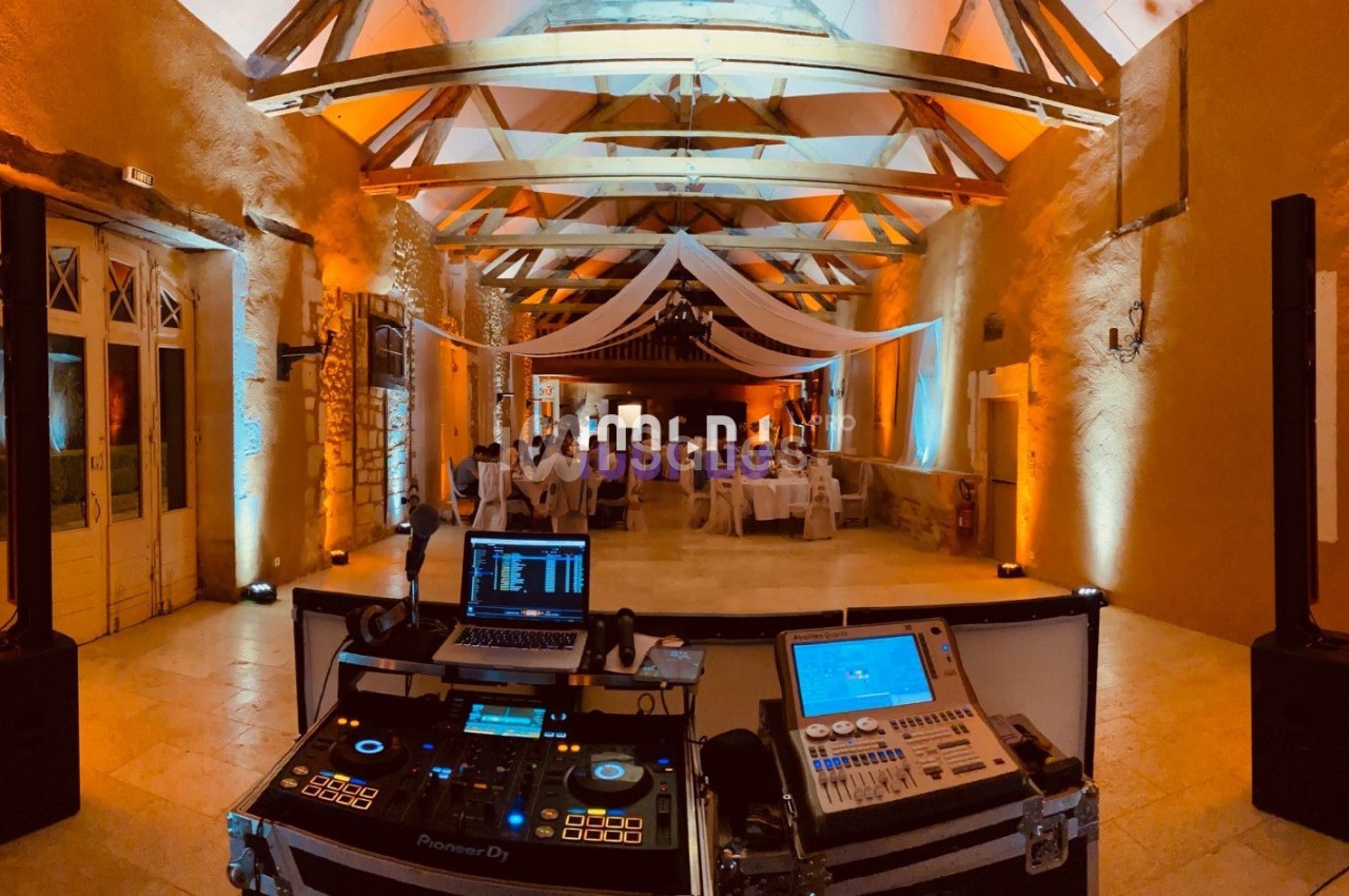 Salle de réception éclairée en orange avec une table de DJ au premier plan et des tables dressées en arrière-plan.