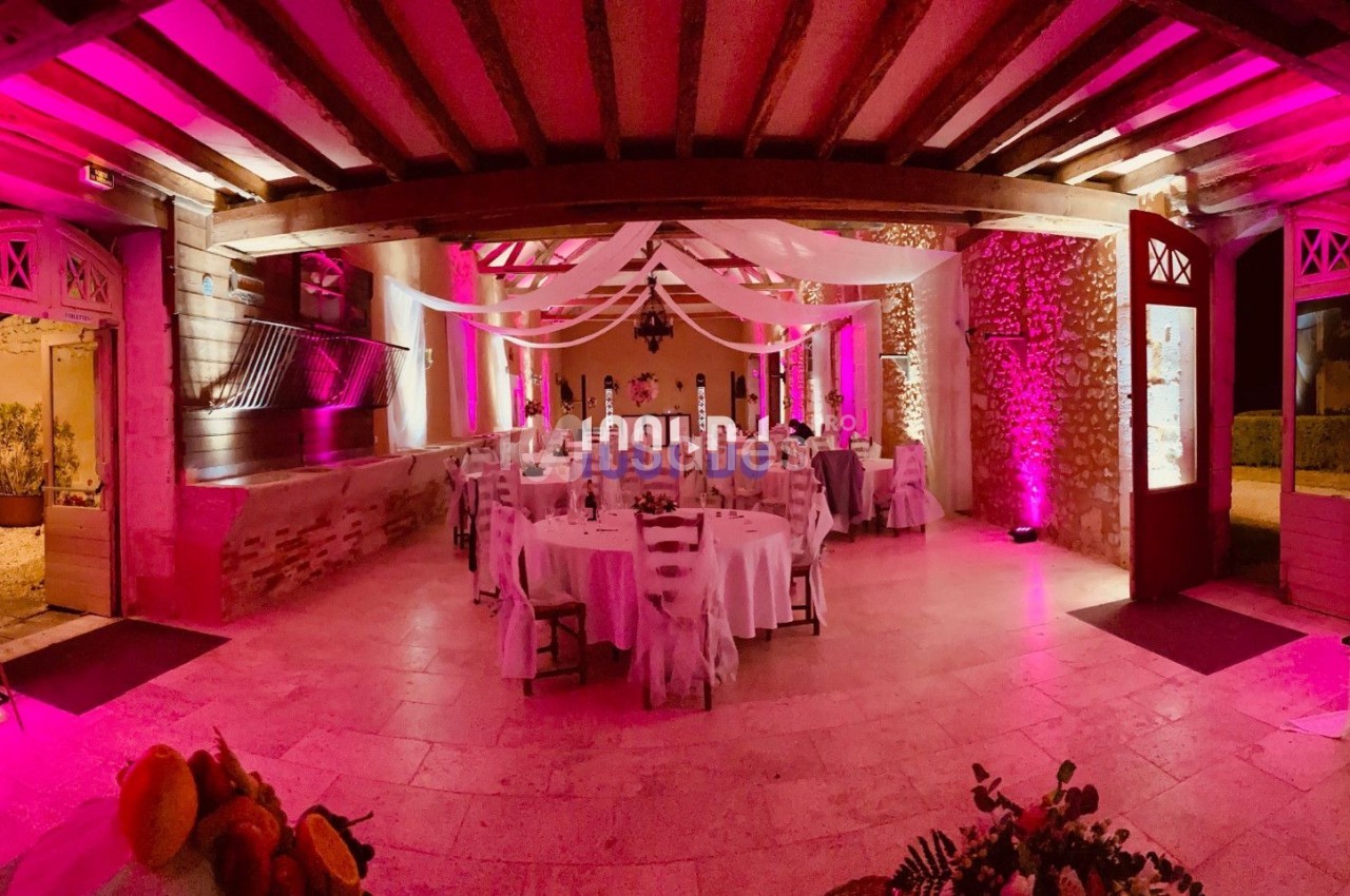 Salle de réception décorée avec des nappes blanches, des guirlandes lumineuses et un éclairage rose.