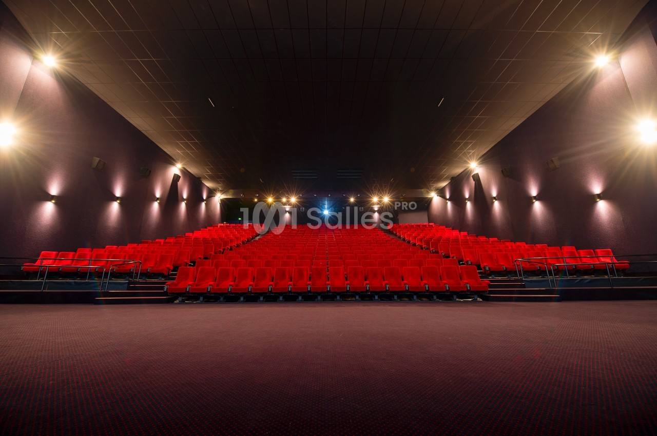 Salle de cinéma vide avec rangées de sièges rouges, éclairage tamisé et écran non visible à l'avant.