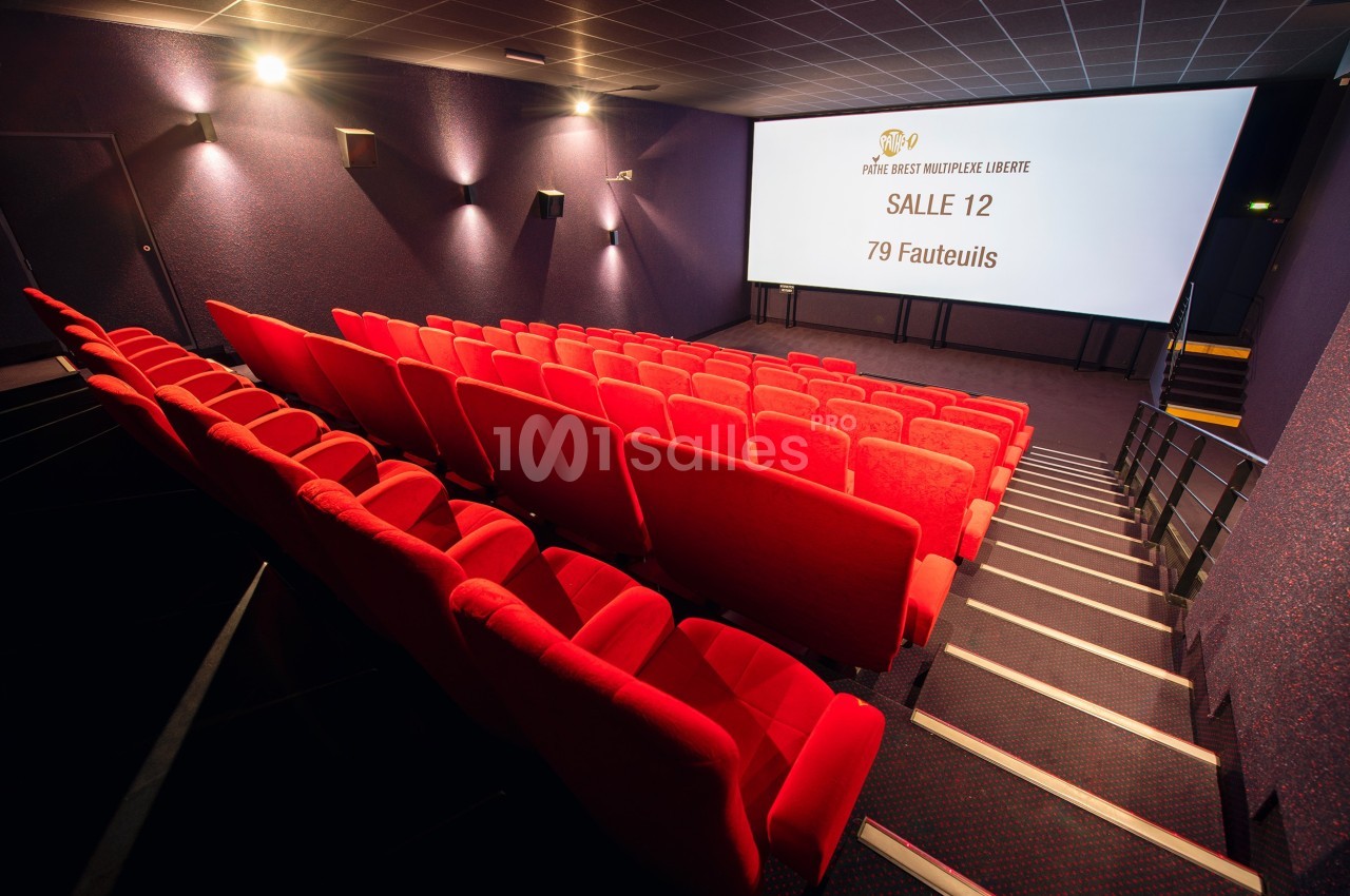 Salle de cinéma vide avec des rangées de fauteuils rouges et un écran affichant ’Salle 12, 79 fauteuils’.