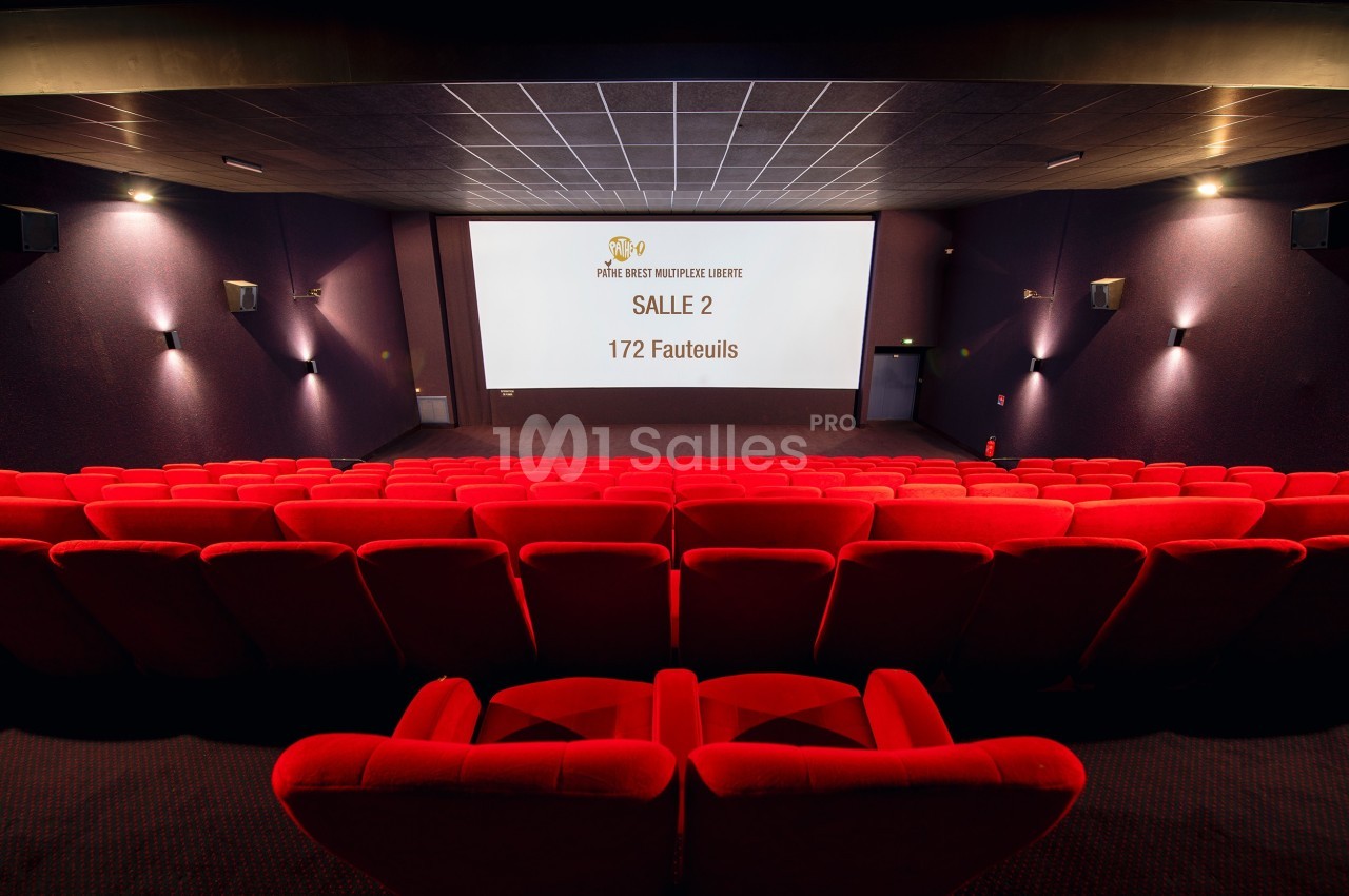Salle de cinéma vide avec des fauteuils rouges, un écran affichant ’Salle 2, 172 fauteuils’ et un éclairage tamisé.