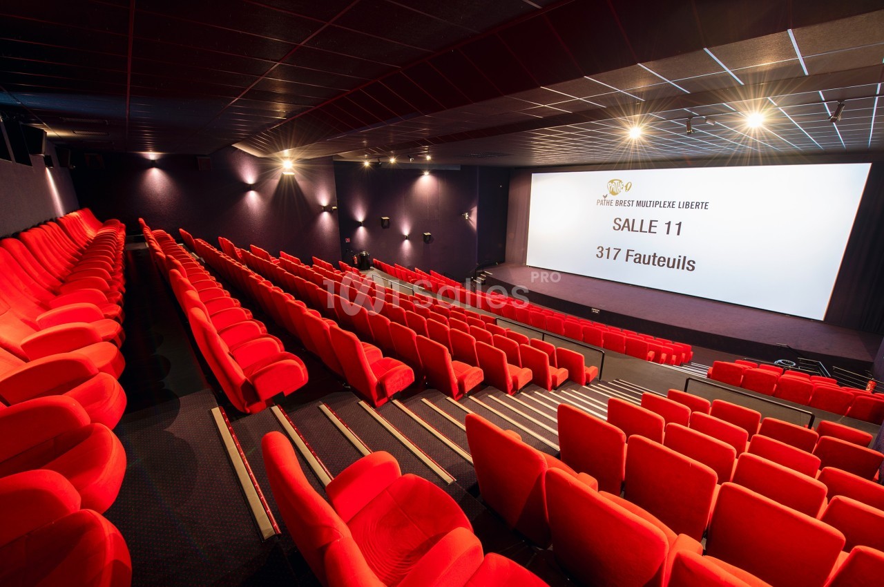 Salle de cinéma vide avec des rangées de fauteuils rouges et un grand écran affichant des informations sur la salle.