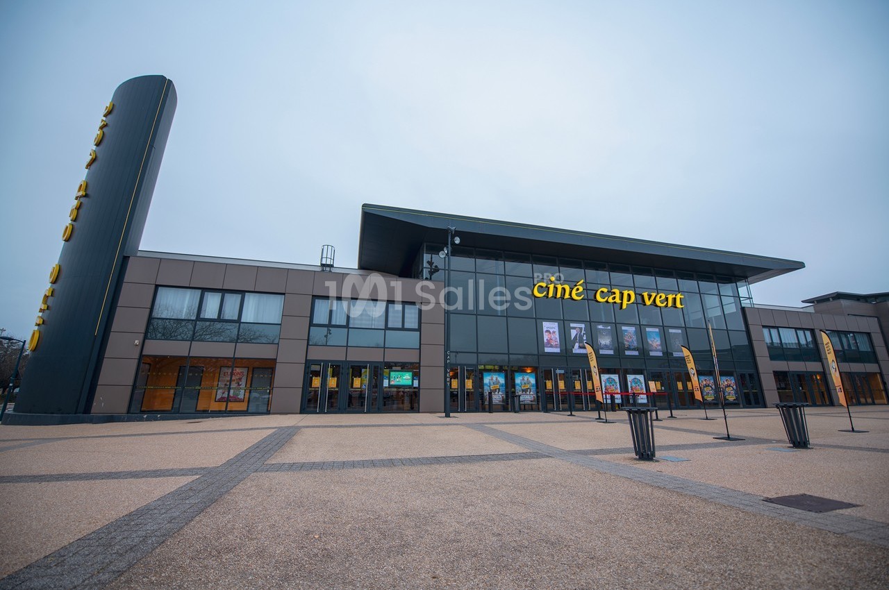 Façade moderne d'un cinéma avec enseigne ’Ciné Cap Vert’, grandes baies vitrées et esplanade dégagée au premier plan.