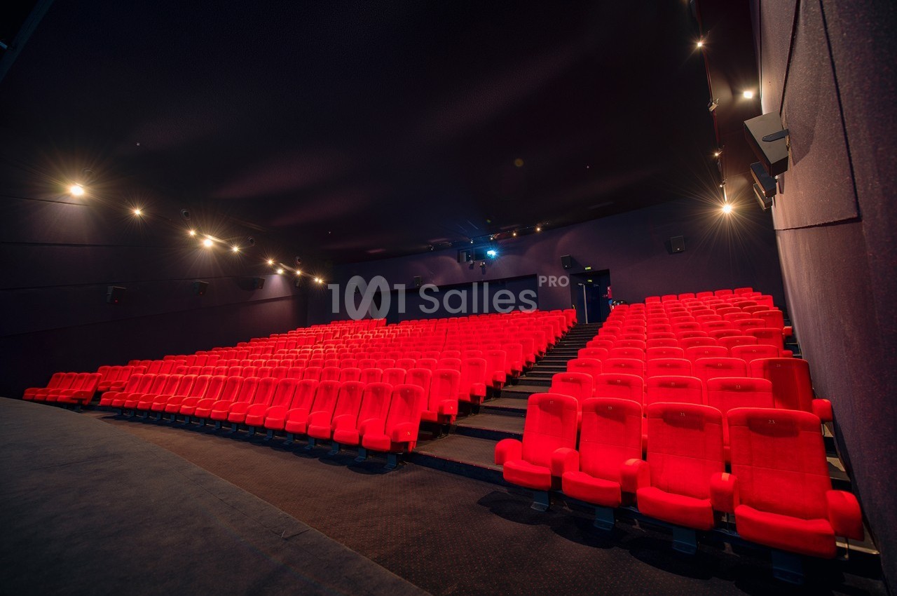 Salle de cinéma vide avec des rangées de sièges rouges et un éclairage tamisé.