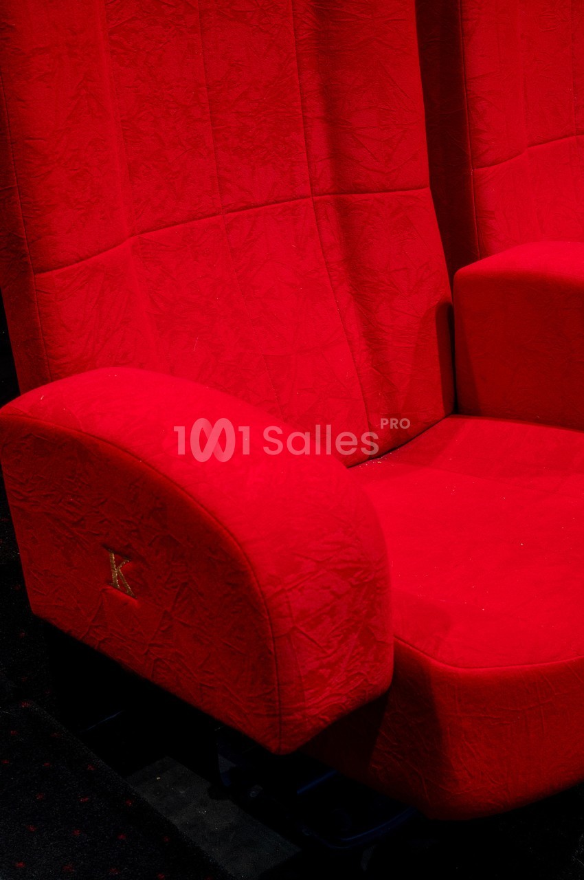 Fauteuil de cinéma rouge avec accoudoirs, placé sur un sol sombre.