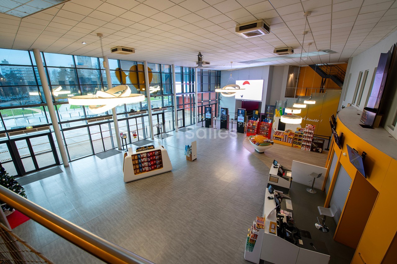 Vue d'un hall spacieux avec comptoir d'accueil, étagères de produits et grandes baies vitrées donnant sur l'extérieur.