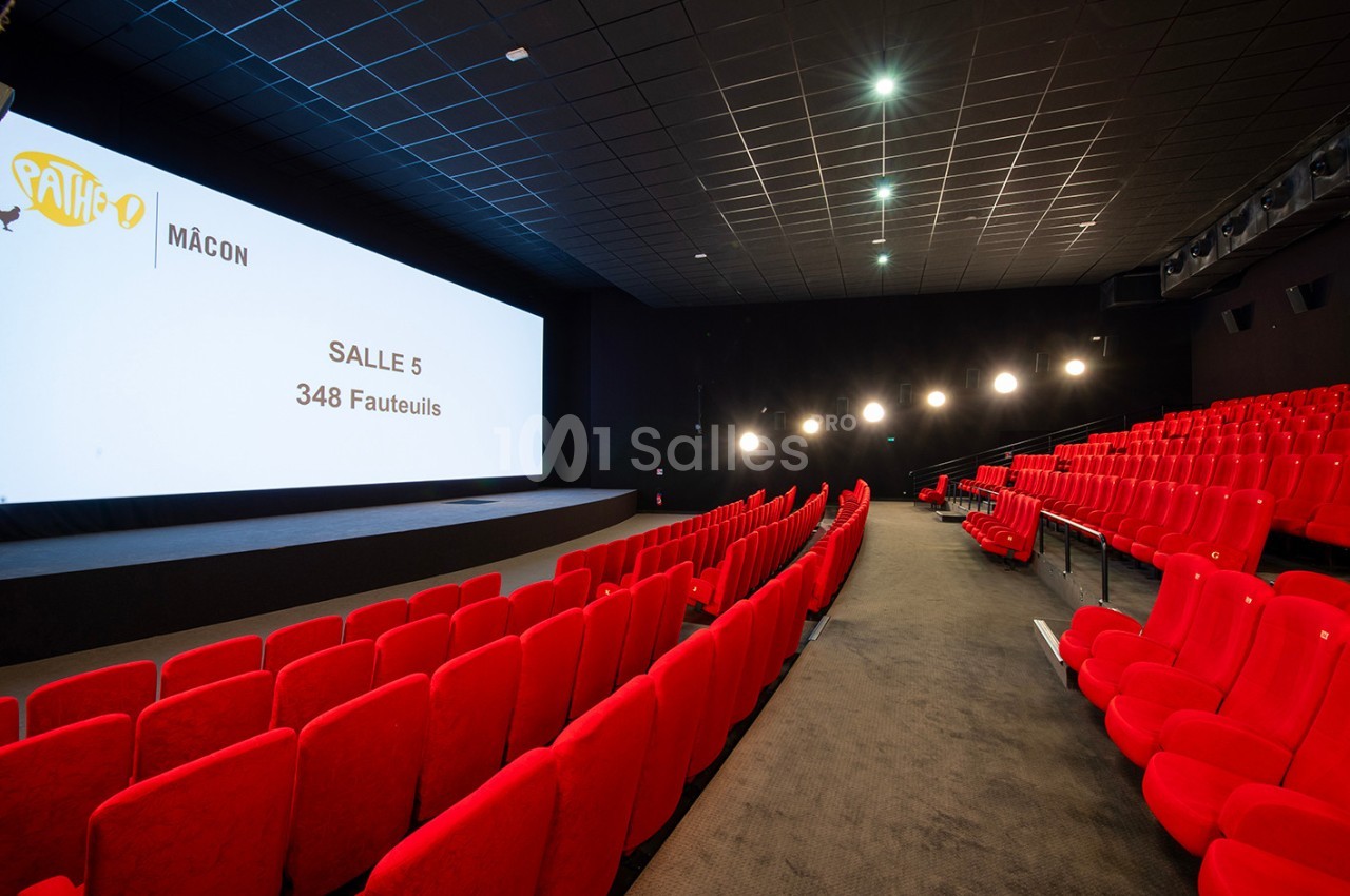 Salle de cinéma avec des rangées de fauteuils rouges vides, écran affichant ’Salle 5, 348 fauteuils’.