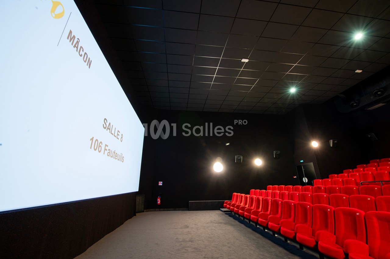 Salle de cinéma avec rangées de sièges rouges, écran blanc affichant ’Salle 8 - 106 fauteuils’ et éclairage tamisé.