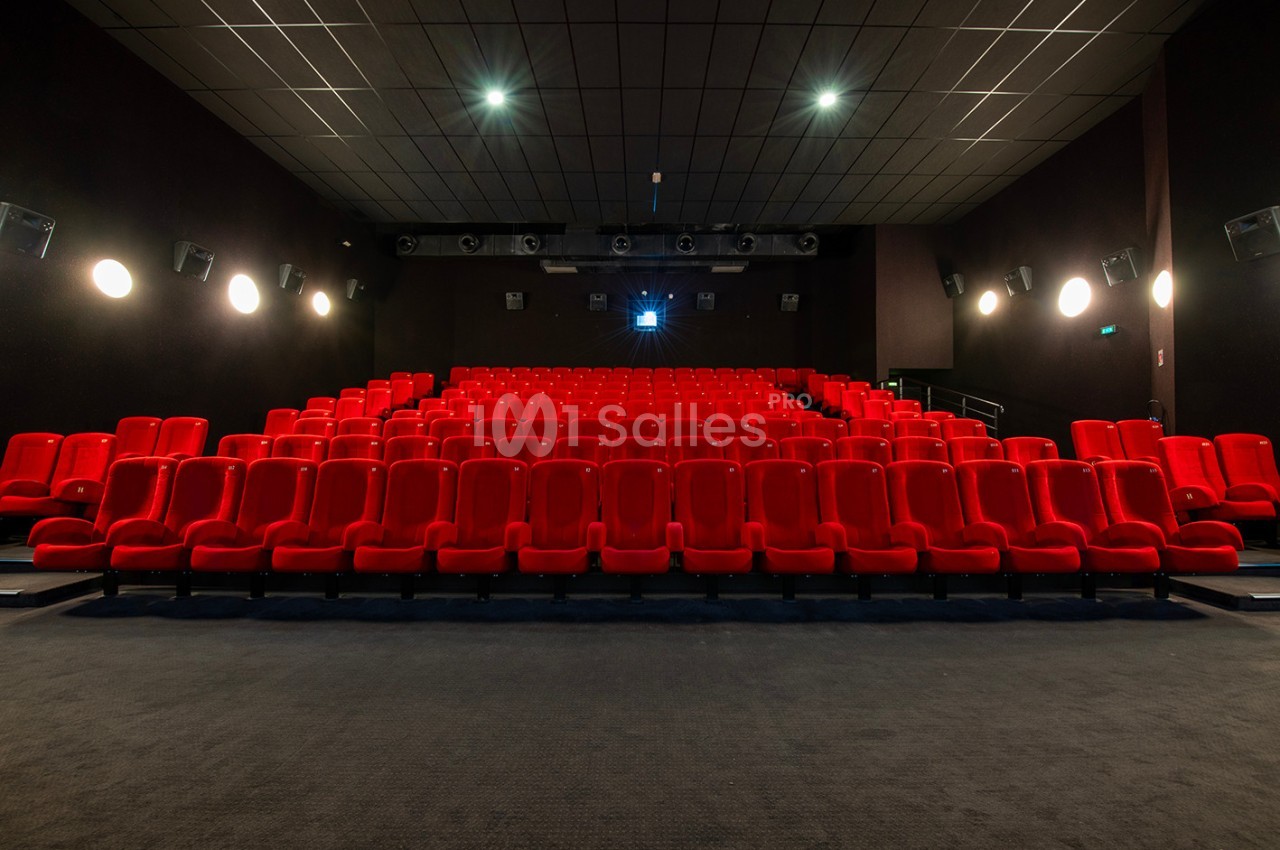 Salle de cinéma vide avec des rangées de sièges rouges et un écran éteint en arrière-plan.
