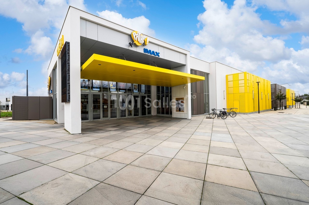 Façade d'un cinéma moderne avec enseigne IMAX, entrée vitrée et auvent jaune, entourée d'un espace pavé.