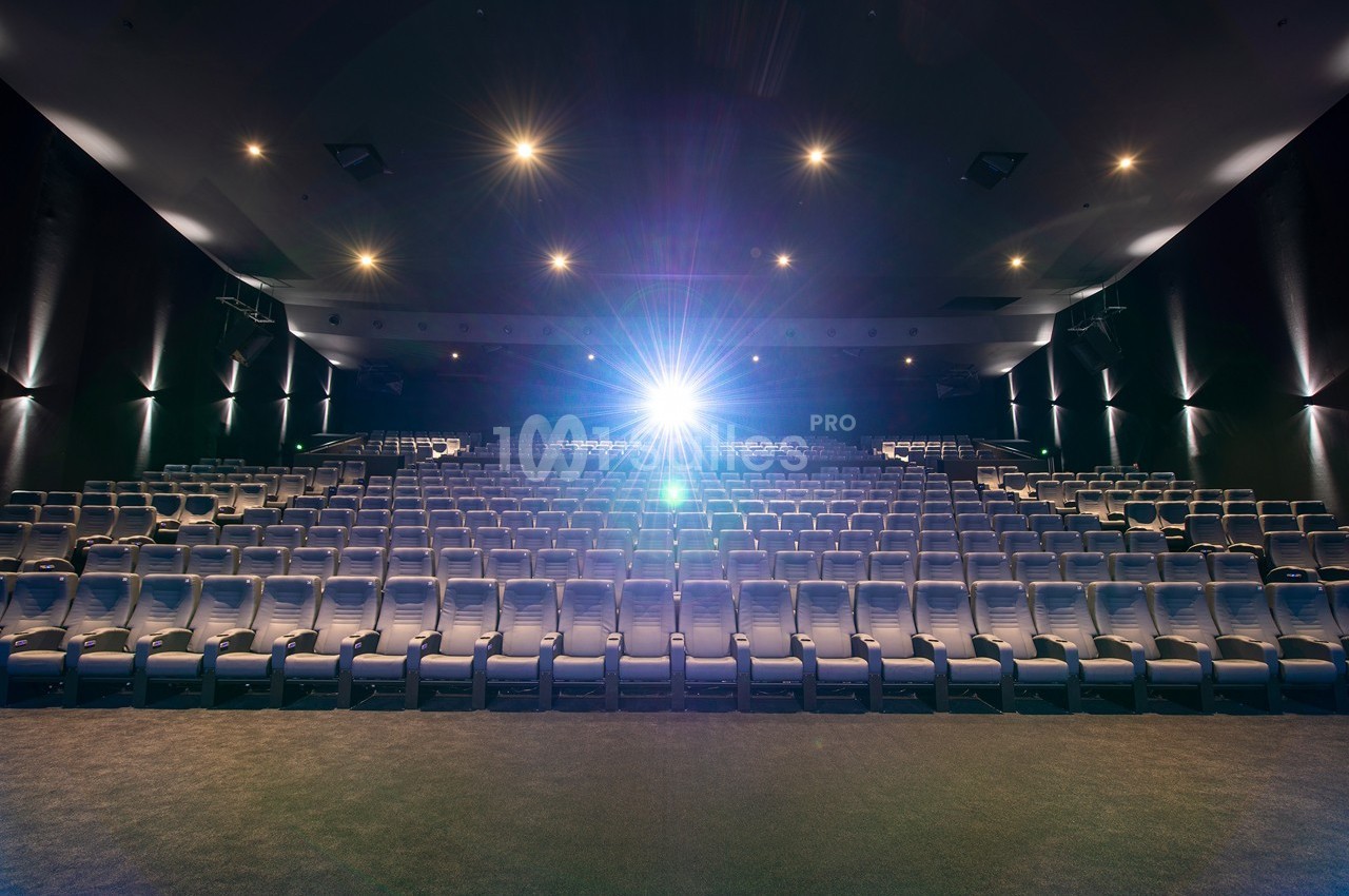Salle de cinéma vide avec des rangées de sièges alignés et un projecteur allumé au fond.