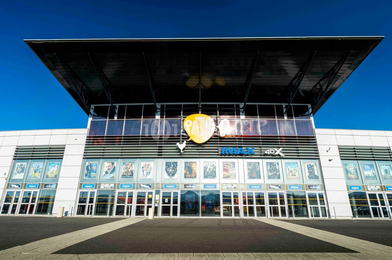 Façade d'un cinéma moderne avec affiches de films visibles sur les vitrines et un grand logo central.