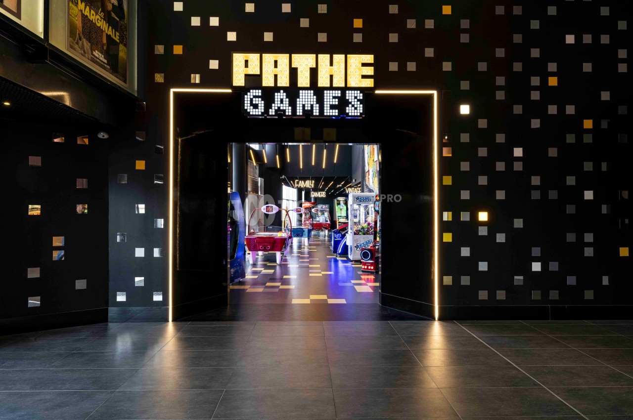 Entrée d'une salle d'arcade lumineuse avec enseigne ’Pathé Games’ et jeux visibles à l'intérieur.