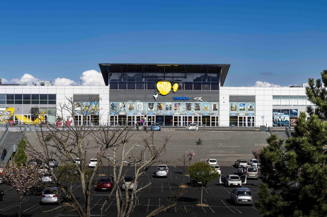 Façade d'un cinéma avec un parking au premier plan, quelques arbres et un ciel dégagé en arrière-plan.