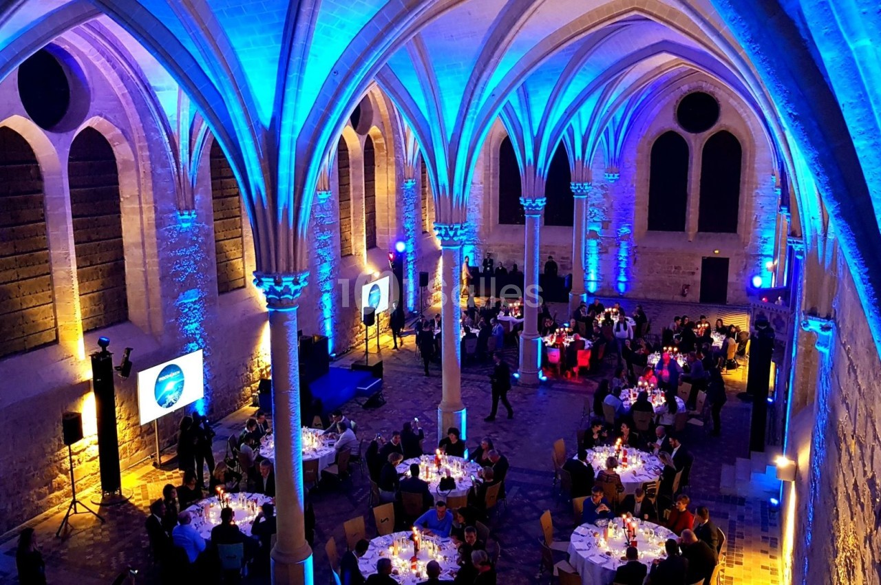 Salle voûtée éclairée en bleu accueillant un dîner avec des tables rondes dressées et des convives assis.