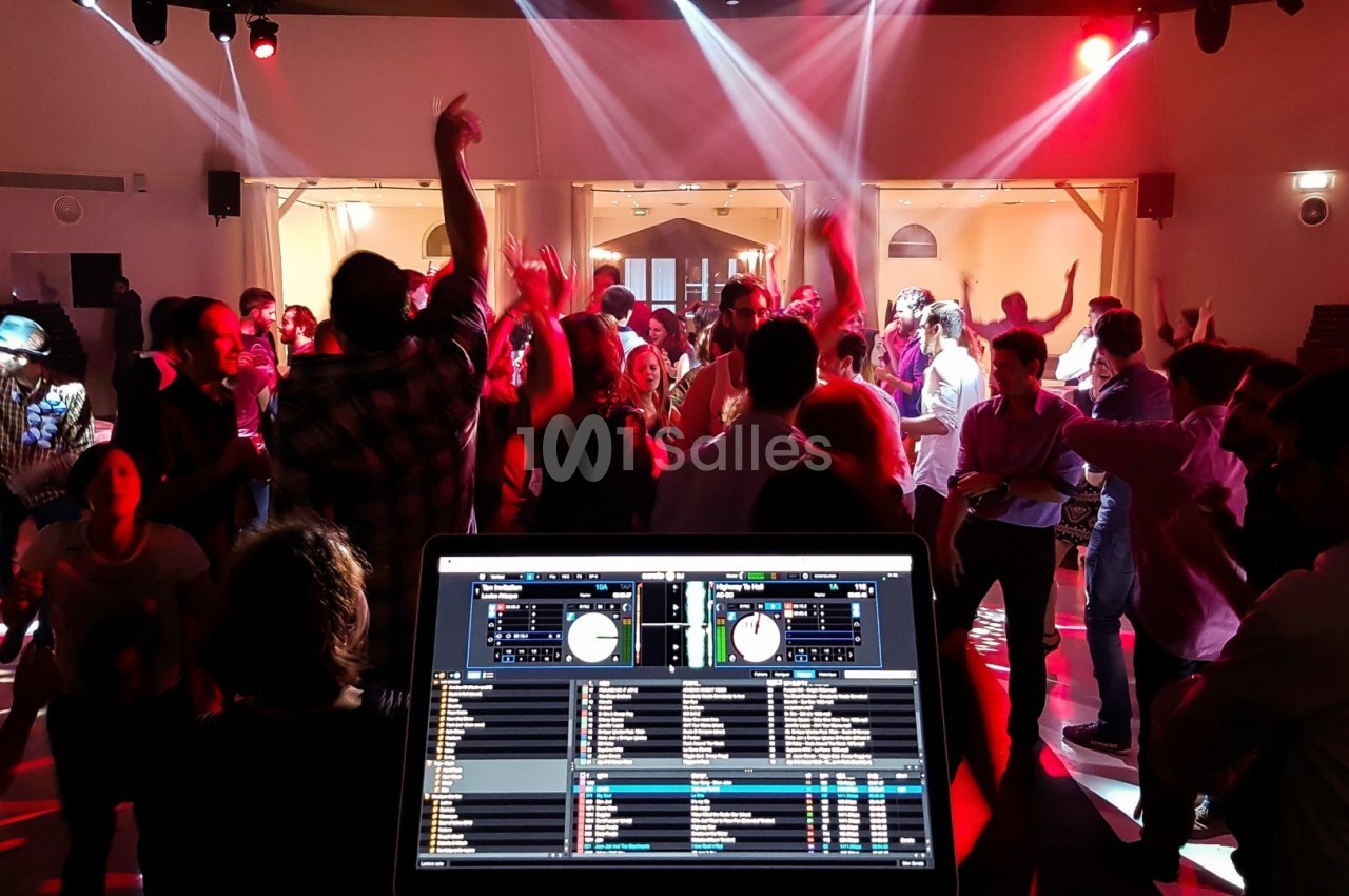 Vue d'une fête avec des personnes dansant sous des lumières colorées, écran de DJ en premier plan.