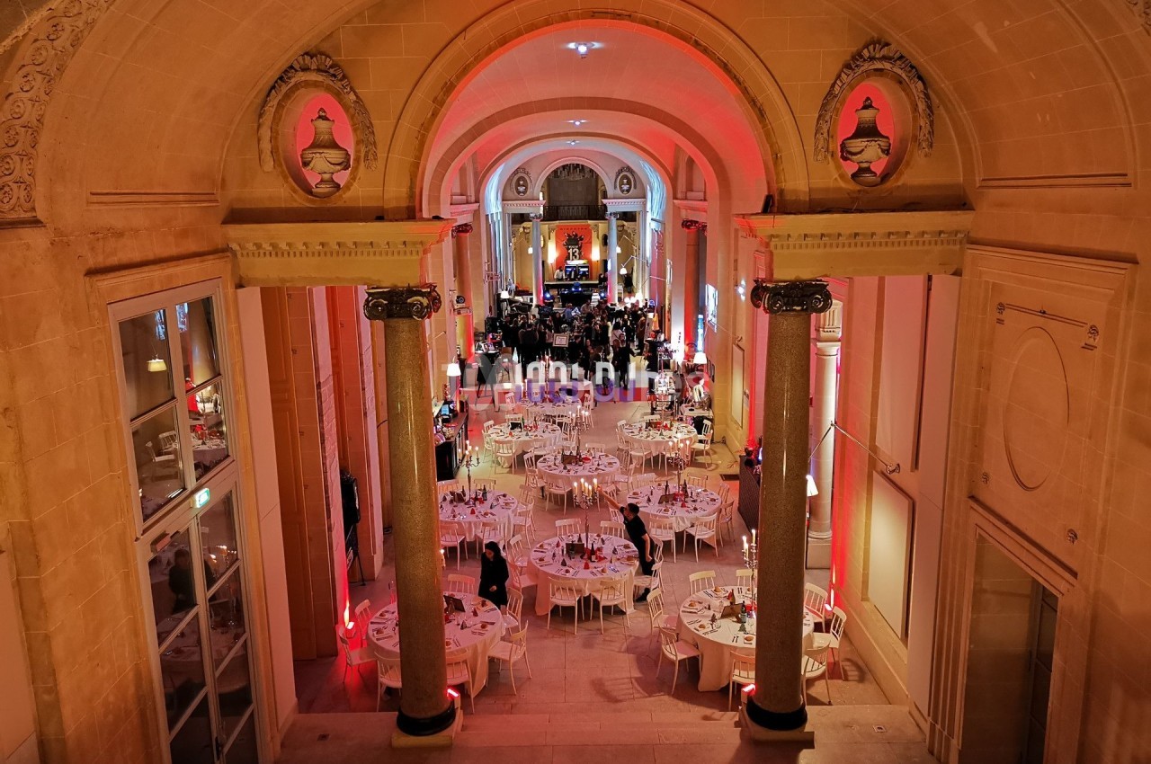 Salle de réception élégante avec tables rondes dressées, éclairage chaleureux et architecture classique.