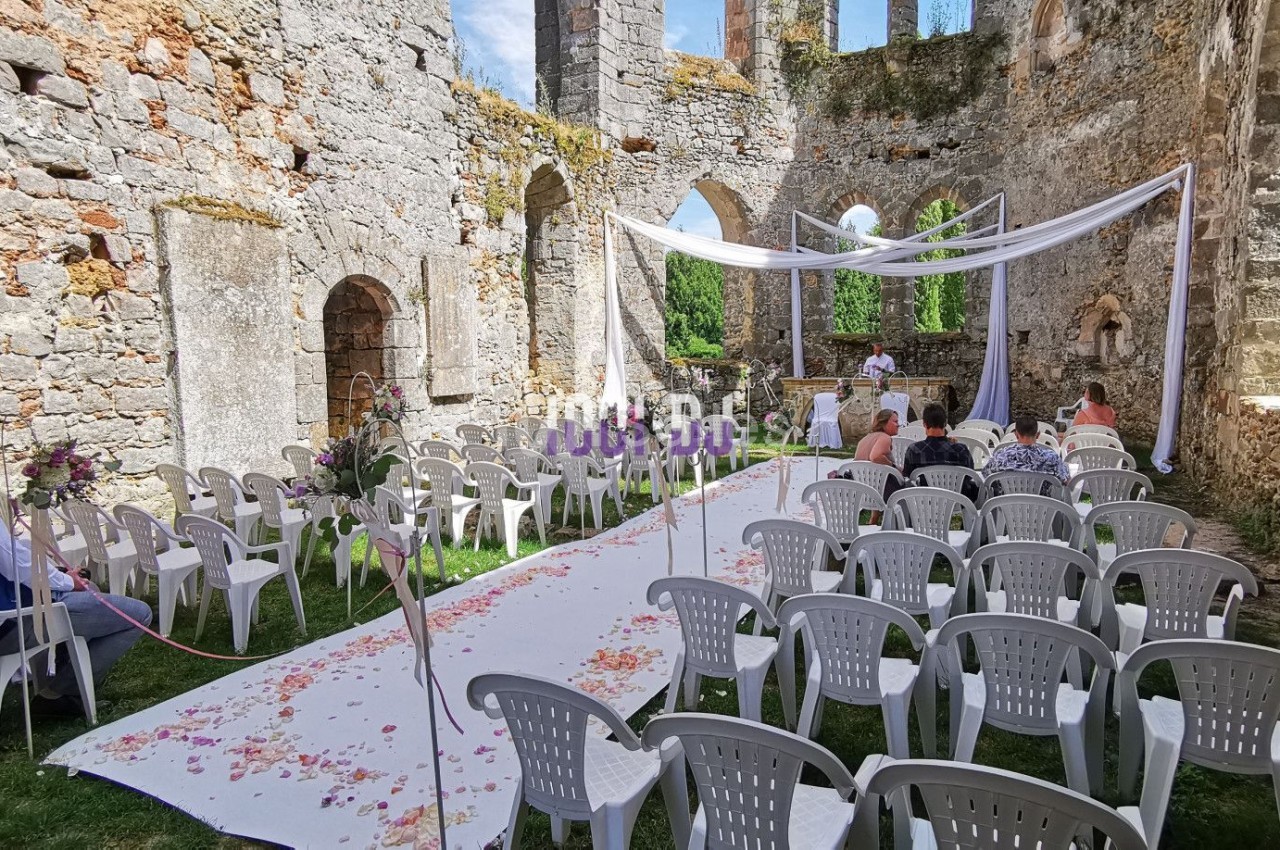 Cérémonie de mariage en plein air dans les ruines d'une église, avec des chaises blanches et une allée décorée de pétales.