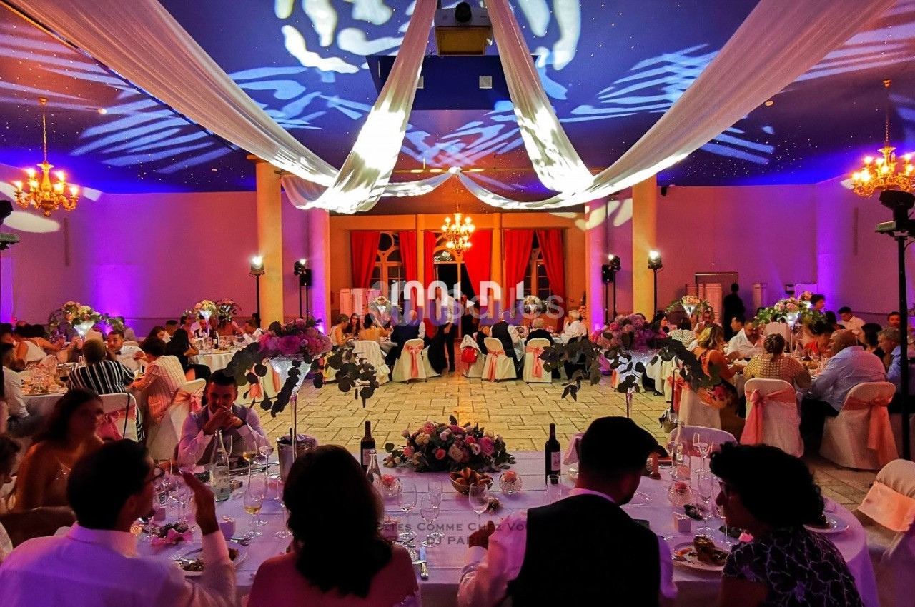 Salle de réception décorée avec des éclairages colorés, des tables dressées et des invités assis lors d'un événement festif.