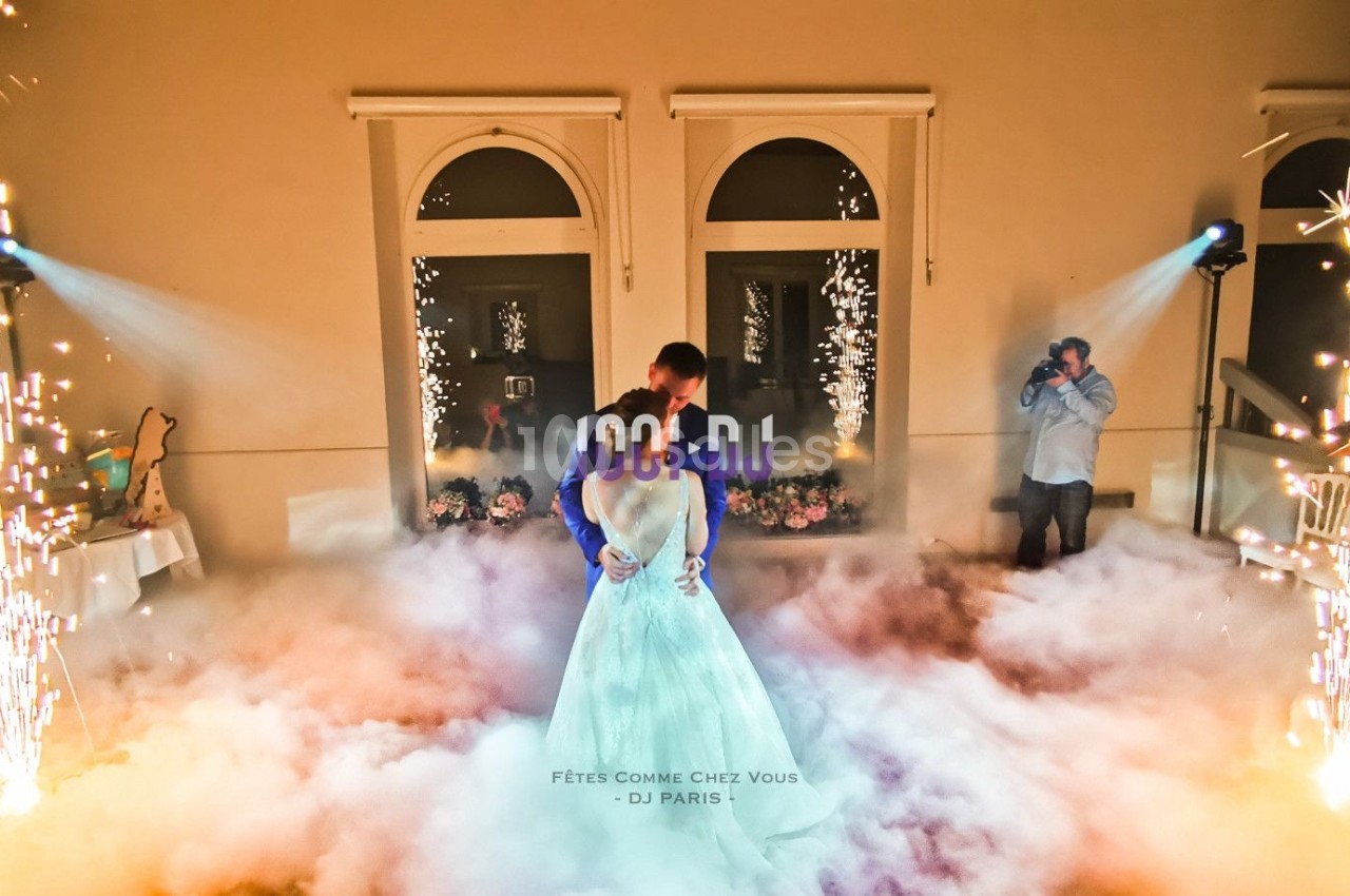 Un couple danse au milieu d'une piste entourée de fumée et d'effets pyrotechniques dans une salle éclairée.