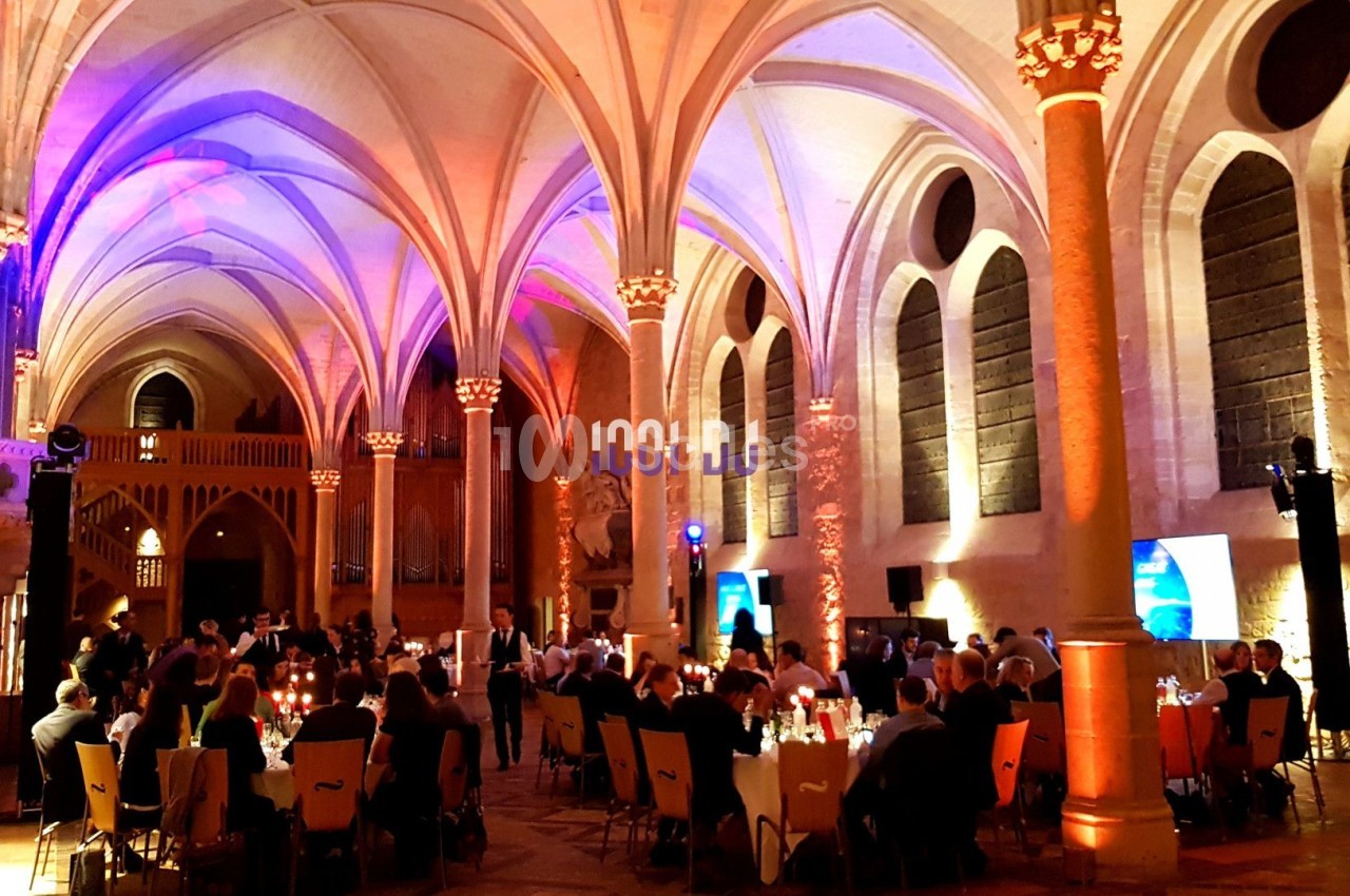 Salle voûtée éclairée avec des invités assis à des tables lors d'un événement ou d'un dîner.