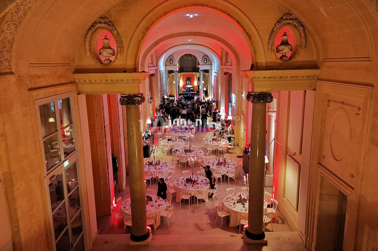 Salle de réception élégante avec tables rondes dressées, éclairage chaleureux et architecture classique.