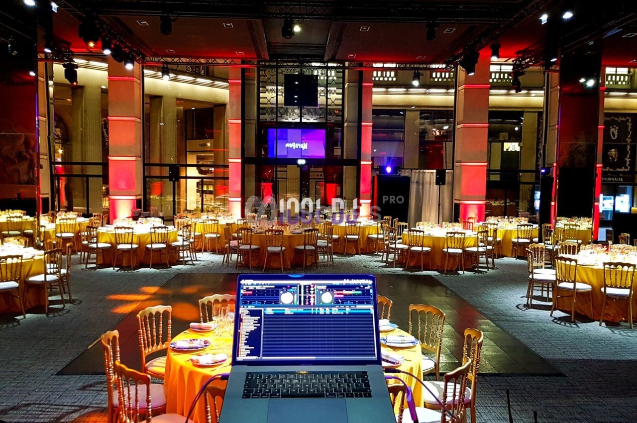 Salle de réception élégamment décorée avec des tables rondes dressées et un ordinateur de DJ au premier plan.