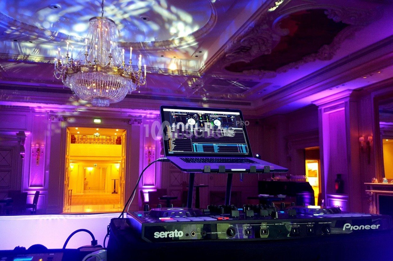 Console de DJ avec ordinateur portable dans une salle élégante éclairée par des lumières colorées et un grand lustre.