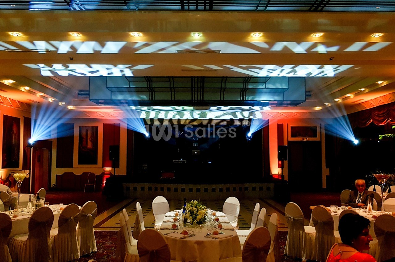Salle de réception décorée avec des tables dressées, éclairages colorés et projecteurs illuminant le plafond.