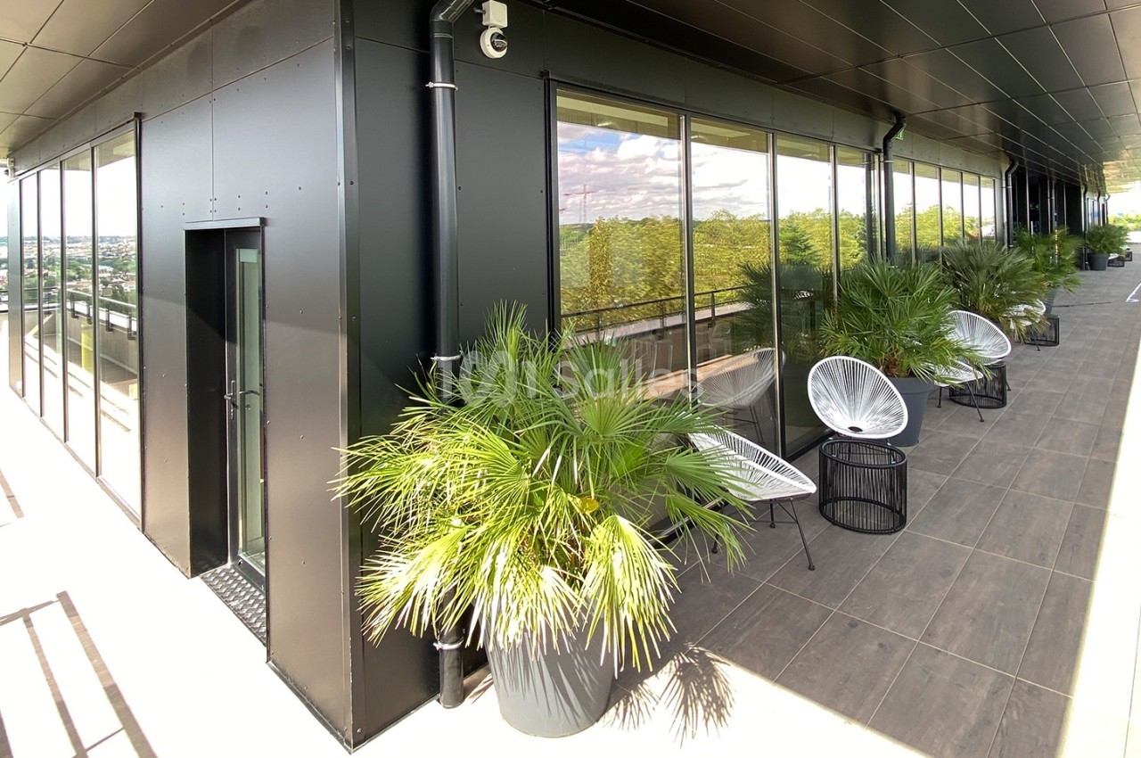 Terrasse moderne avec des plantes en pots, des fauteuils et une vue dégagée sur un paysage urbain.
