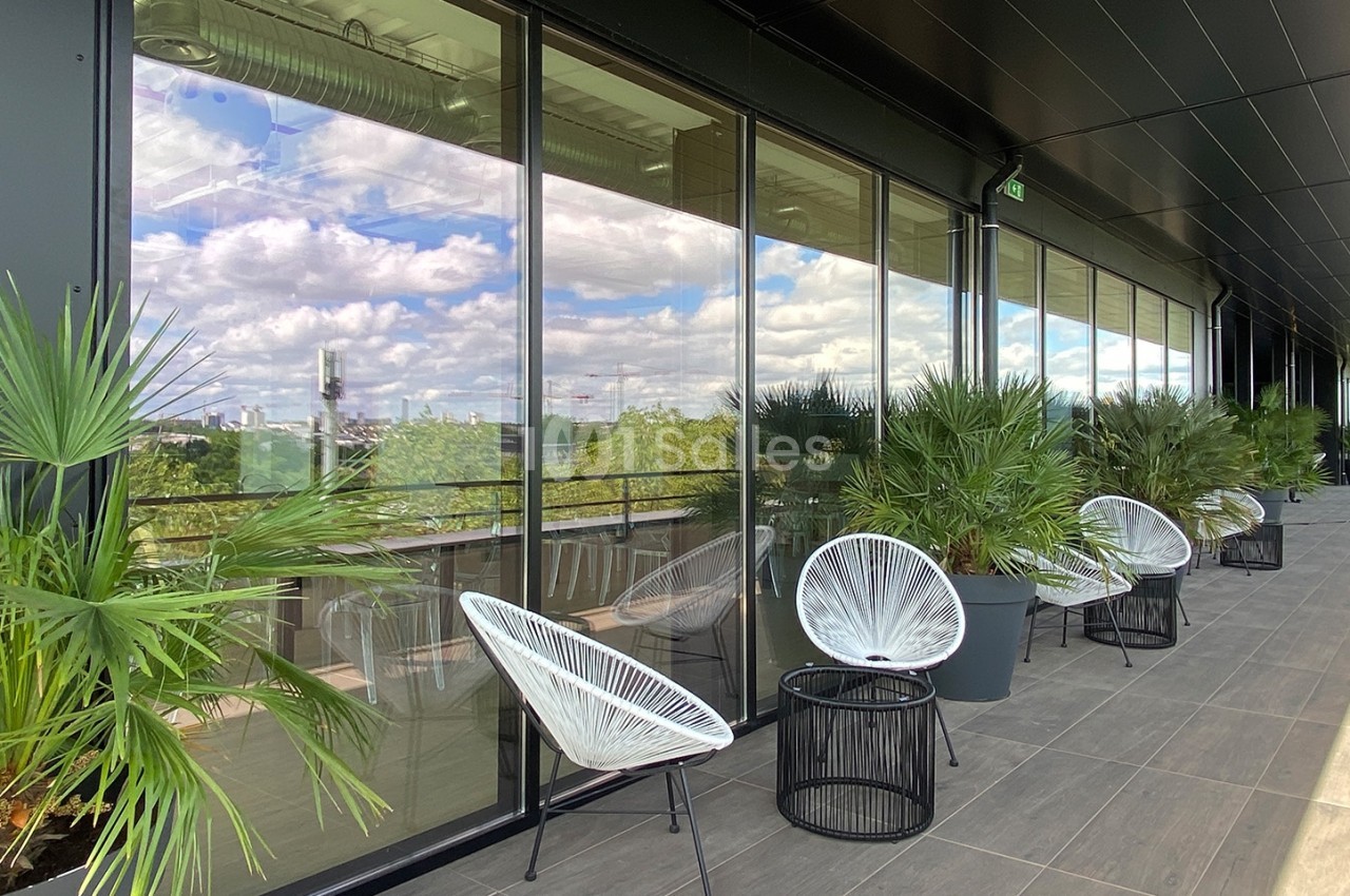 Terrasse moderne avec fauteuils design, tables basses et plantes, offrant une vue dégagée sur un paysage urbain.